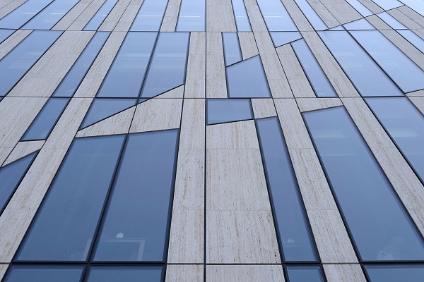 L'eterogenea facciata nasce dalla una griglia modulare caratterizzata dal diverso ordine di elementi complanari di grandezza differente, composti da travertino e vetro.